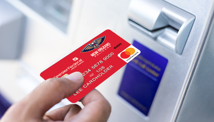 A hand placing a Mardi Gras themed Keesler debit card into an ATM machine.
